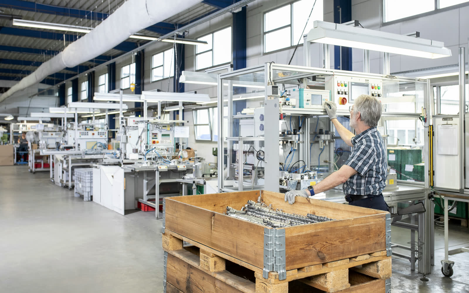 Mitarbeiter bedient Prüfanlage zur Dichtheitsprüfung metallischer Bauteile in heller Fertigungshalle