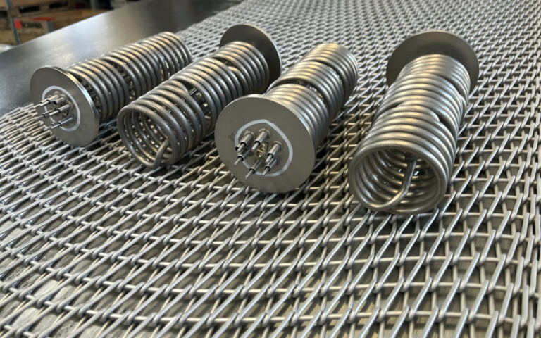 Four stainless steel heater assemblies with tube coils and flange plates, produced by controlled-atmosphere brazing