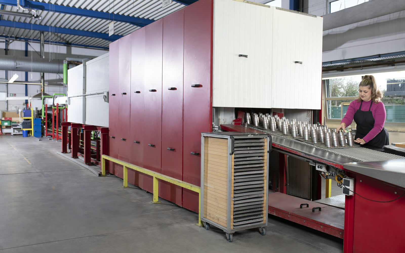Mitarbeiterin bestückt Förderband eines Schutzgasofens mit metallischen Bauteilen zum Schutzgaslöten