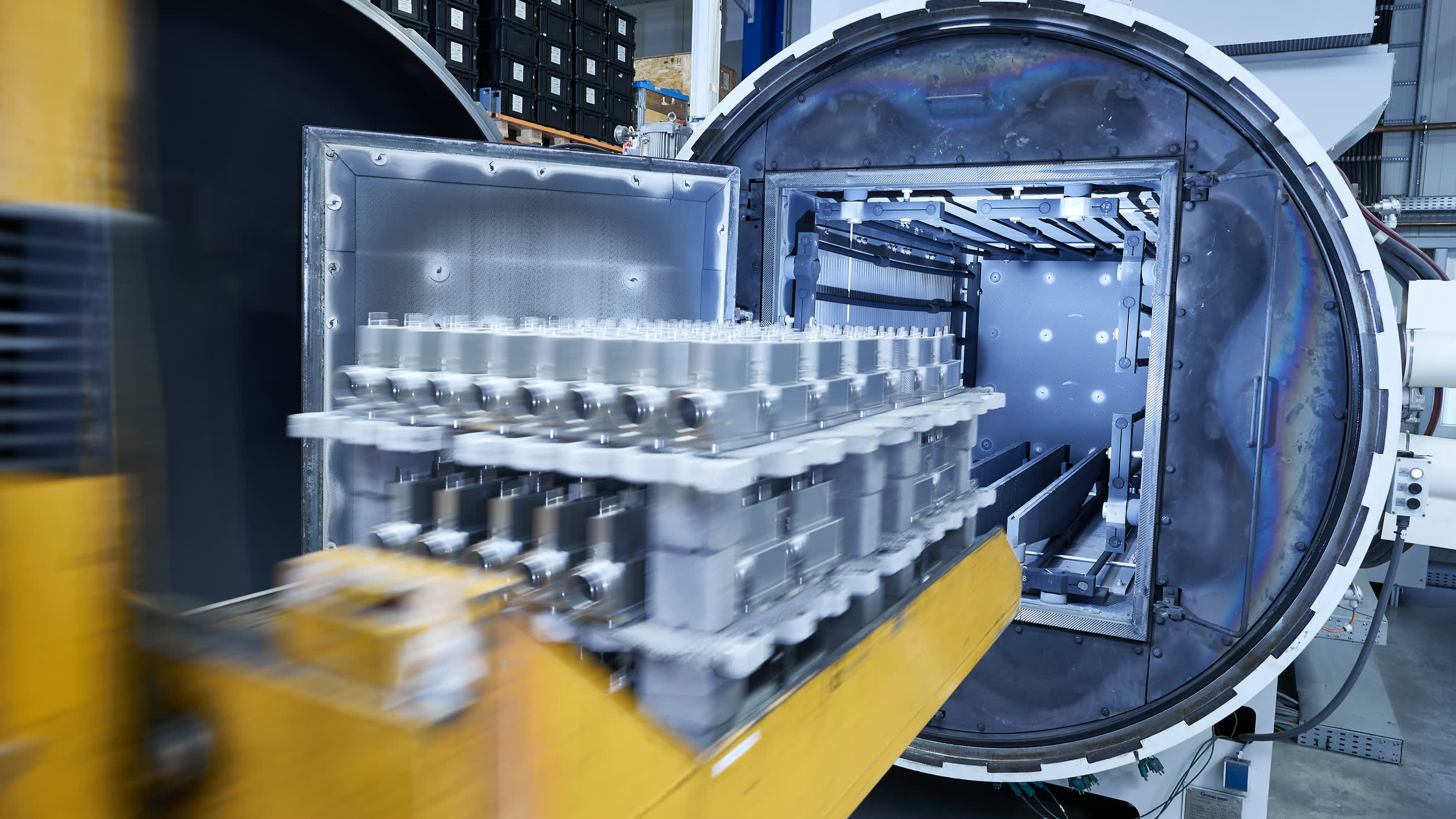 Geöffneter Vakuumofen mit Chargengestell voller Metallbauteile zum Vakuumlöten in der Fertigungshalle